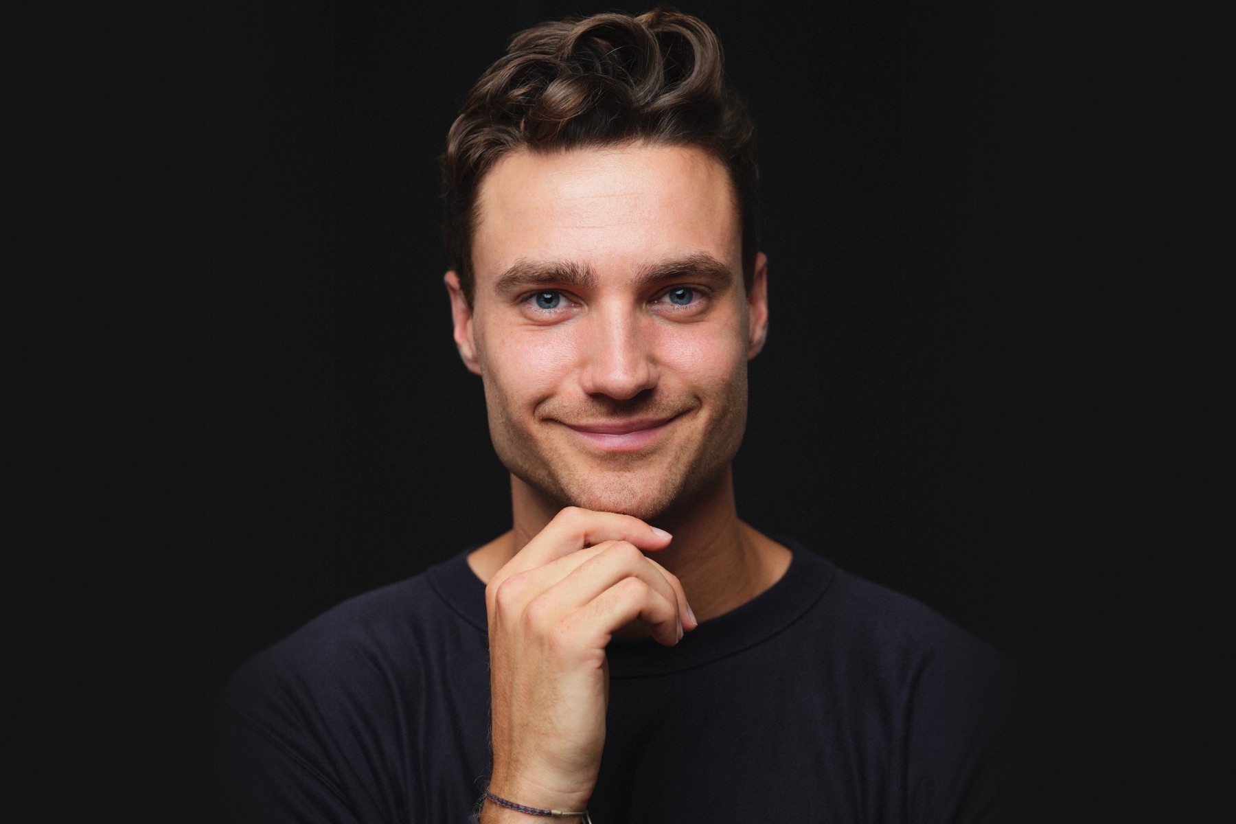 Felix Haas, smiling, his chin resting on his hand, against a dark background